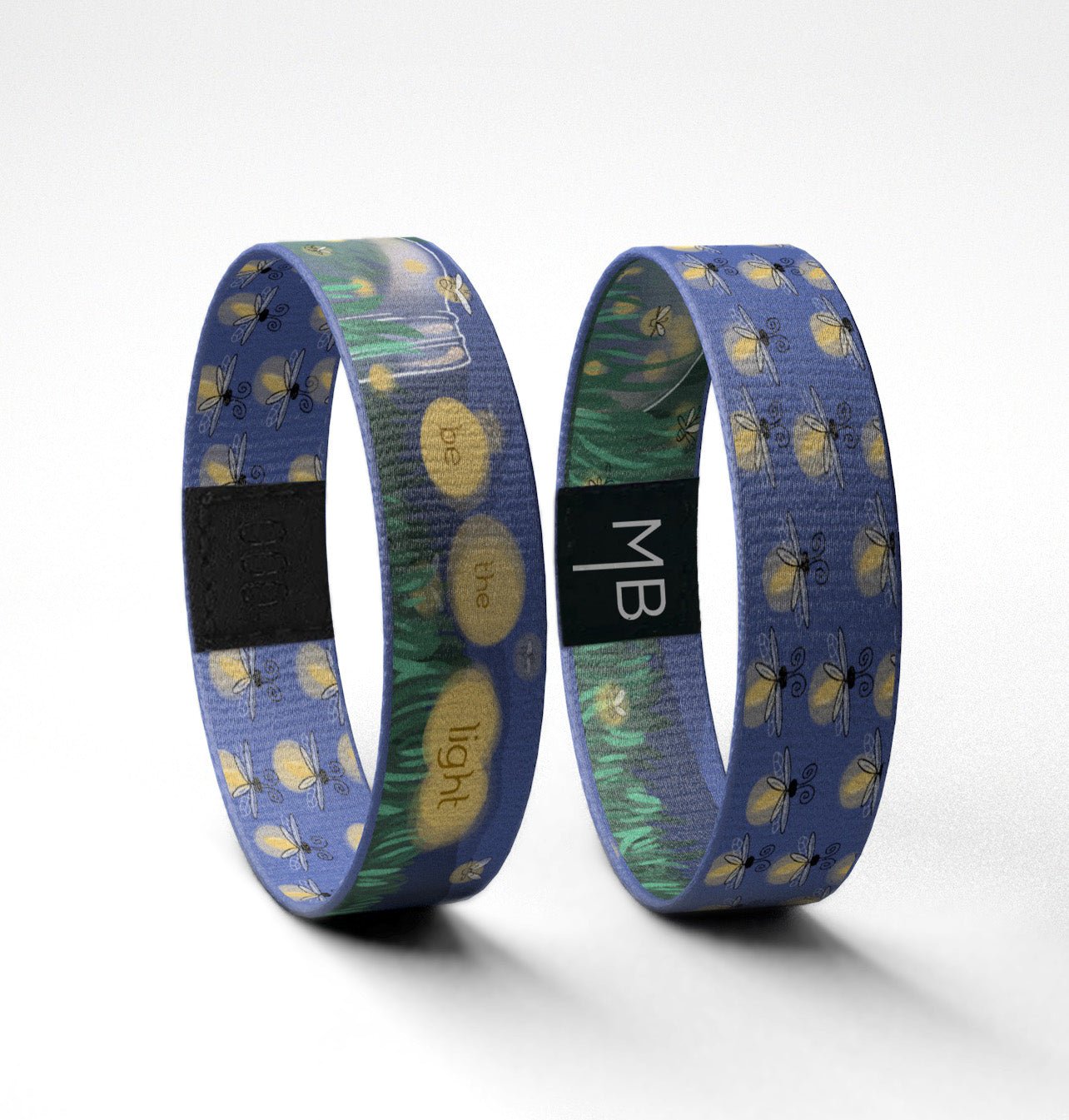 This Moxxie inspirational wristband features little fireflies, or maybe you call them lightning bugs all over in a soft yellow to appear as if they are glowing on a deep cobalt blue background. The text side of this motivational wristband features a Mason jar tipped on its side laying in the grass against a night sky, a grouping of the fireflies illuminates the words “be the light.” The reversible side of this band is cobalt blue and wrapped in a pattern of fireflies. Standing Up View.