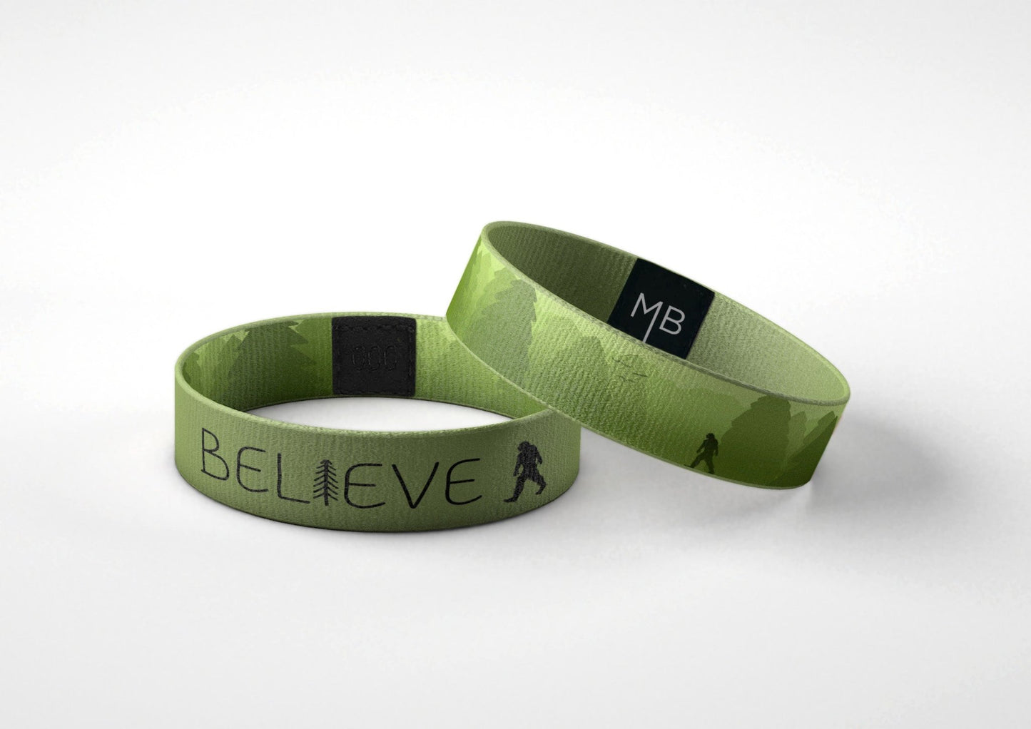 Moxxie motivational wristband "Believe." It’s lush green color offers a calming reminder on either side. The simple, black text on one side, with a little tree detail as a hidden “I” in the message “BELIEVE.” The other side of the wristband is filled with variations of lush green and images of tree filled mountains. There is even a hidden big-foot peeking out from the trees. Laying down view of wristband.